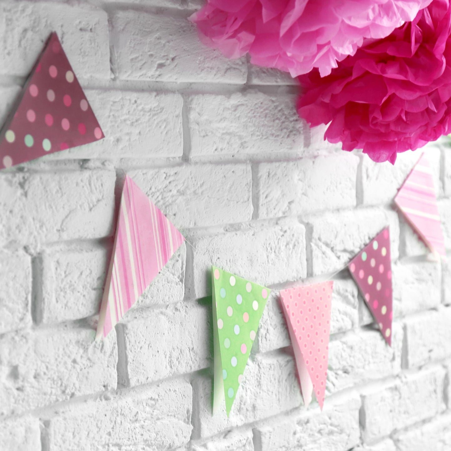 White brick wall with a pastel flag pennant garland and paper flowers