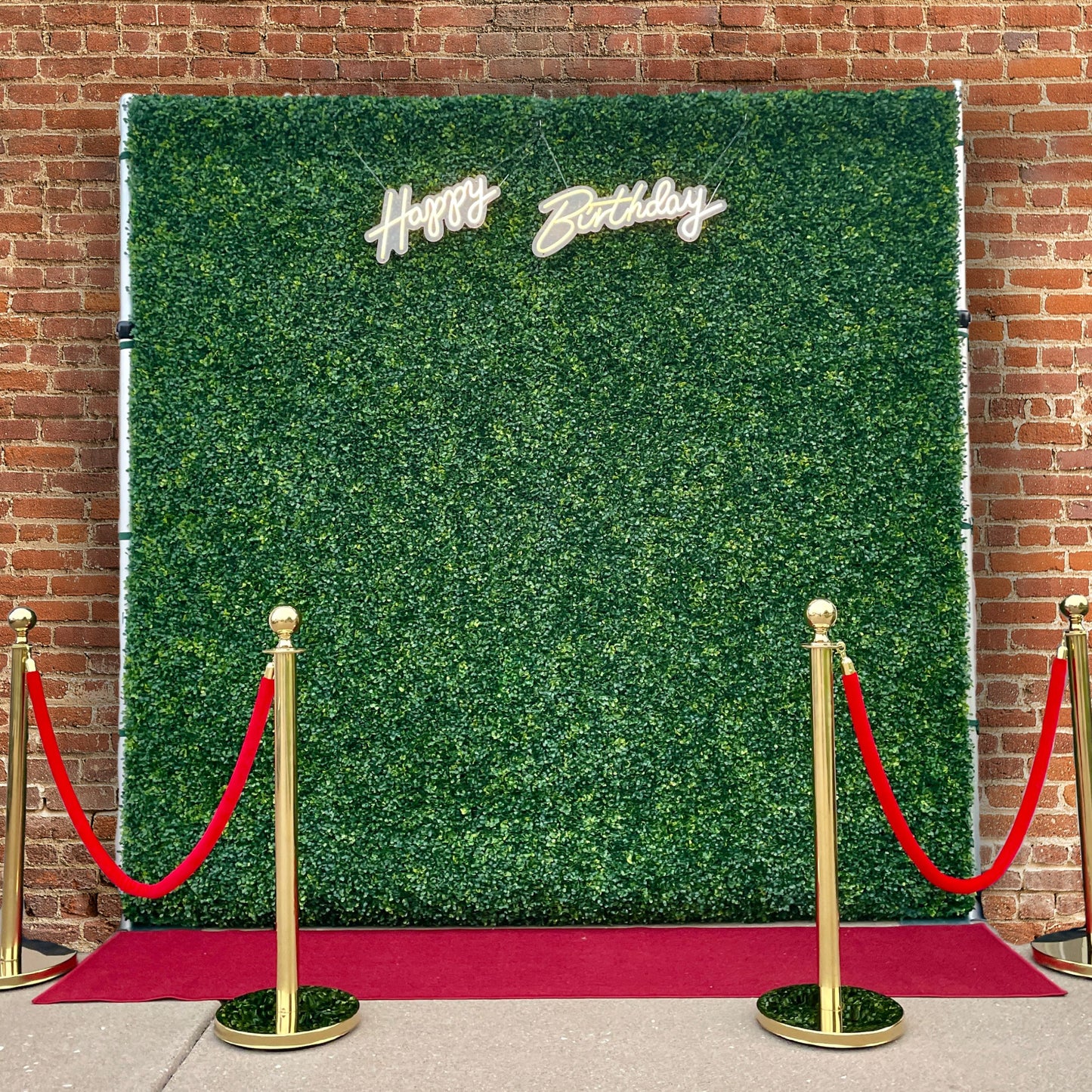 Boxwood wall with a neon happy birthday sign and red carpet velvet ropes and runner
