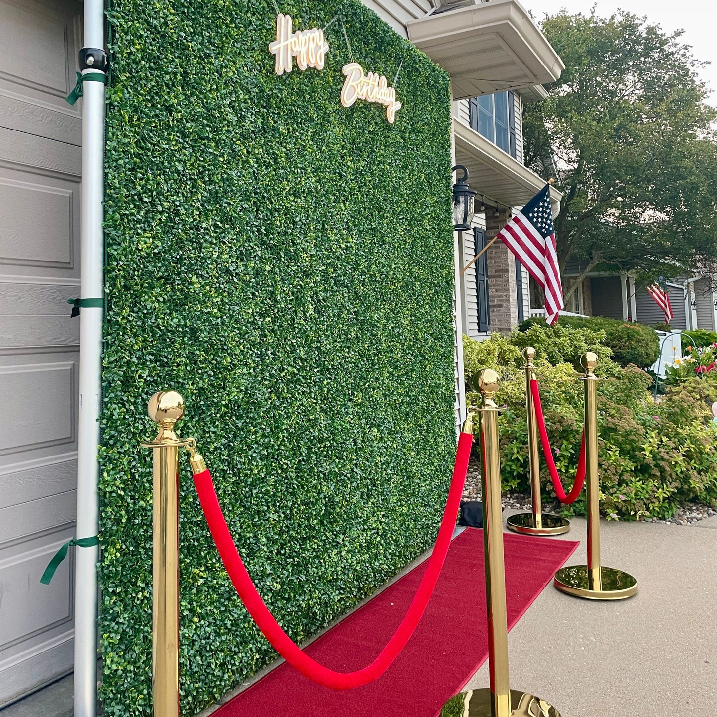 Boxwood wall with red carpet runners and red velvet ropes set up at a residential party
